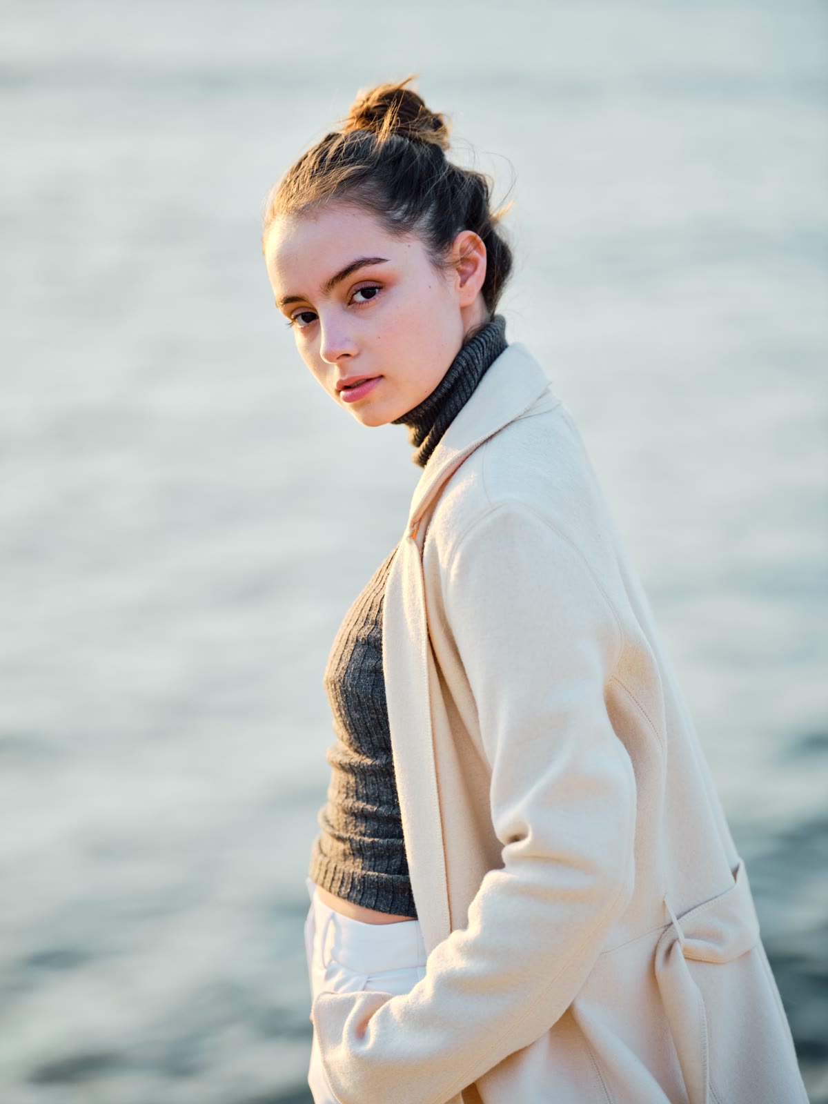 Golden-hour portrait in a cream coat by the water