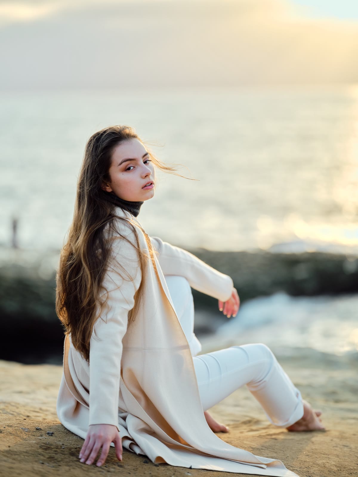 Seated on coastal rocks at sunset, wind in her hair