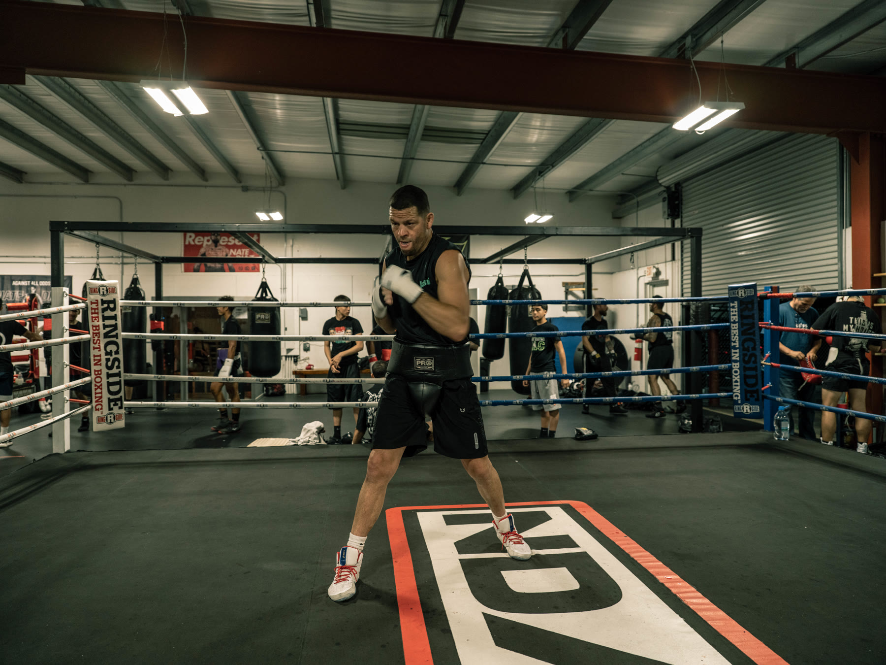 Wide frame of Nate Diaz shadowboxing alone in a boxing ring
